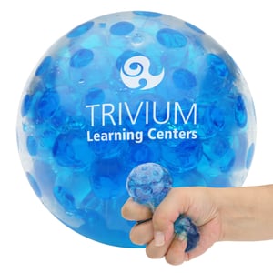 trivium learning center logo on large bead stress ball in background and hand squeezing stress ball in foreground