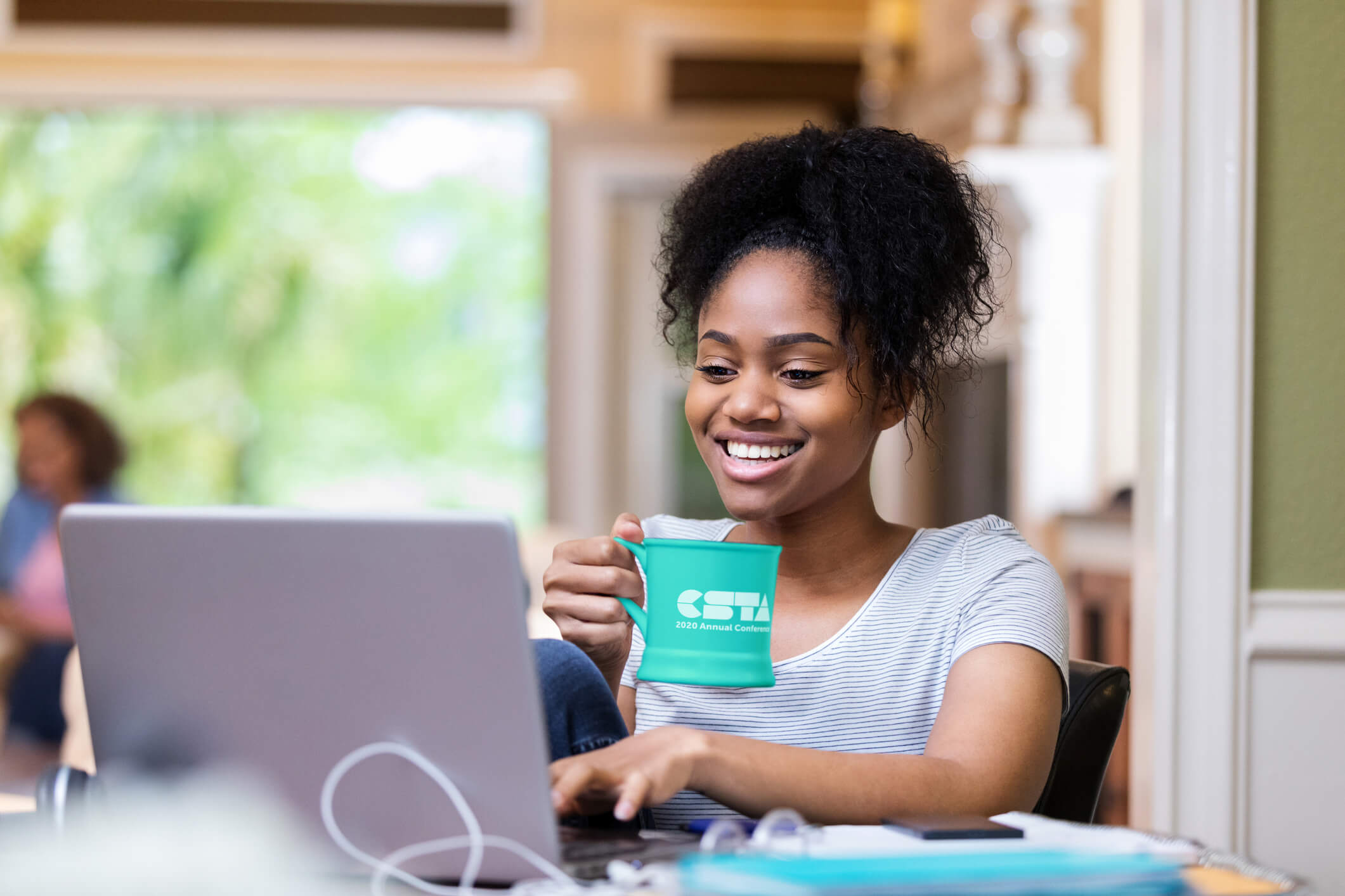 woman sitting at computer holding a green CSTA branded mug